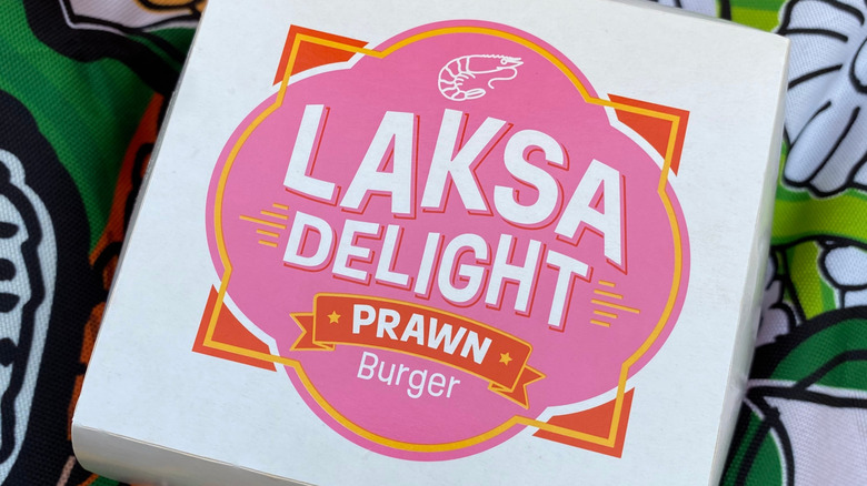 A McDonald's container that reads "Laksa Delight Prawn Burger"