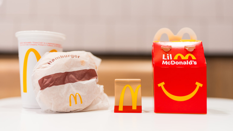 McDonald's hamburger wrapped in paper, drink cup, and Happy Meal box on white surface