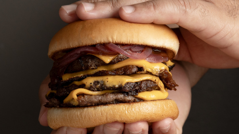 A hand holding a fast food cheeseburger with four patties