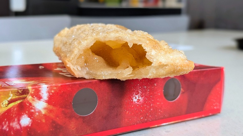 A close-up of a McDonald's Fried Apple Pie with a bite taken out balancing on the box it came in