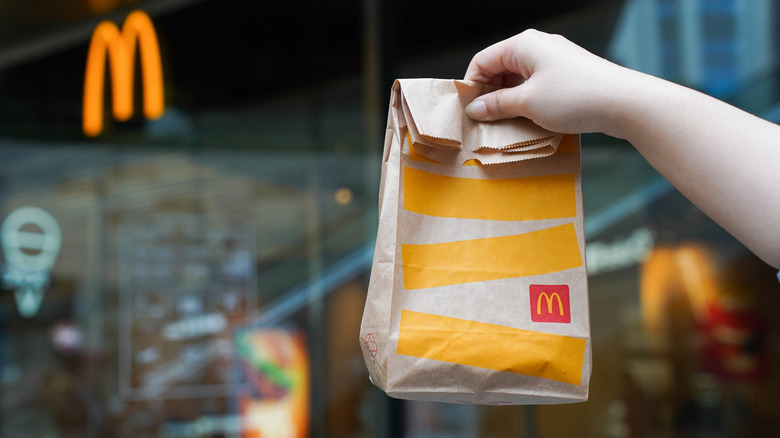 outstretched hand holds McDonald's bag to-go outside restaurant