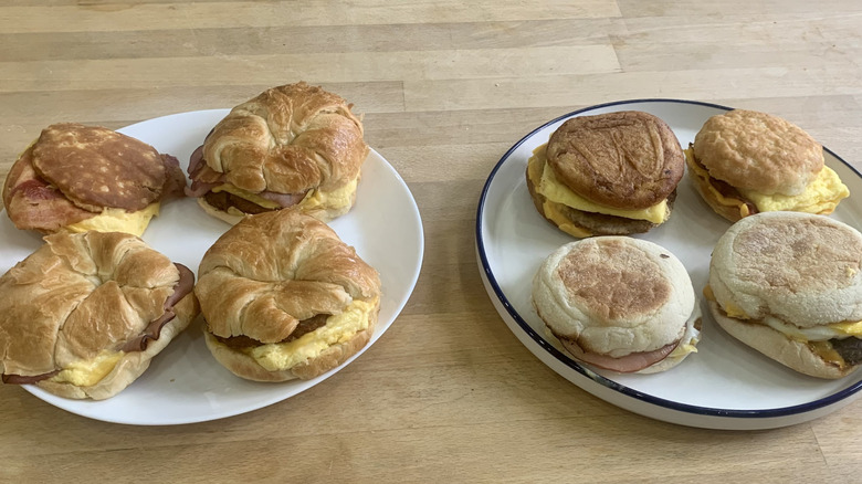 Four Burger King and four McDonald's breakfast sandwiches on plates with wood background