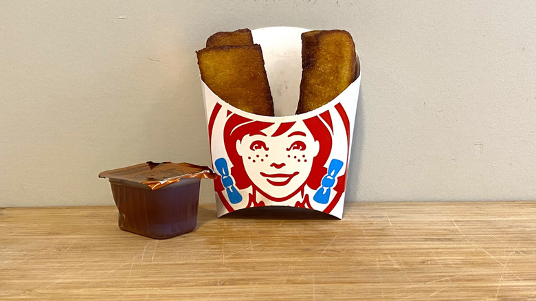 Homestyle French Toast Sticks in a sleeve next to Wendy's maple syrup.