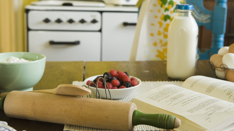 a cookbook and cooking supplies on a table with vintage appliances in the background