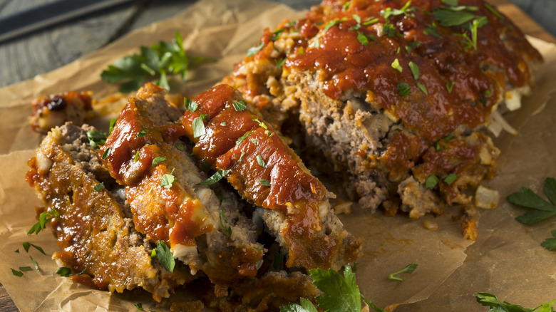 A sliced meatloaf with a tomatoey glaze and fresh herbs on top