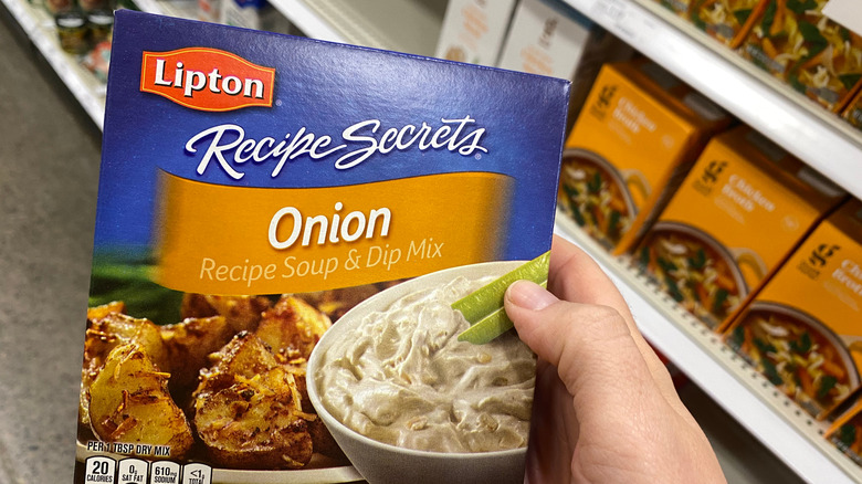 A hand holding a box of Lipton Recipe Secrets onion soup and dip mix
