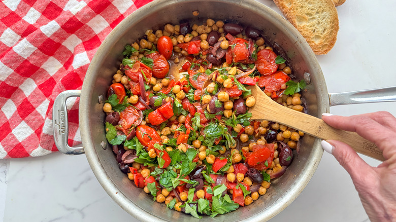 Wooden spoon holding scoopful of Mediterranean chickpea skillet