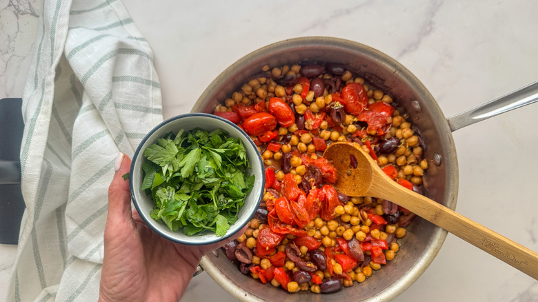 hand adding parsley to pan