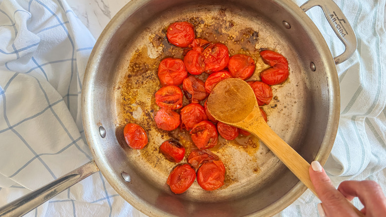 hand smashing tomatoes in pan