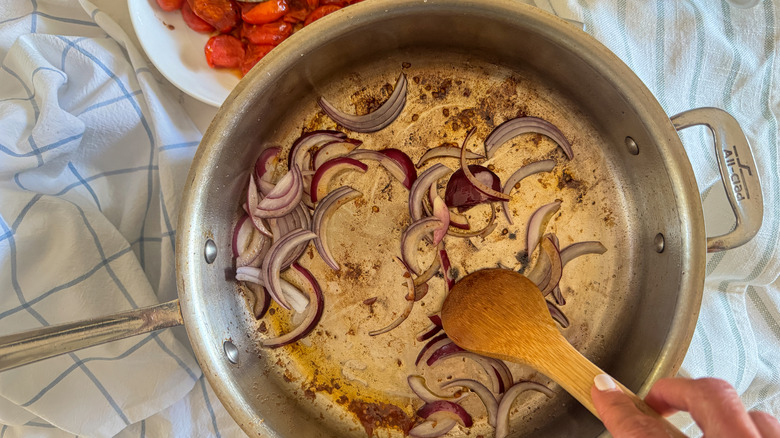 hand stirring onion in pan