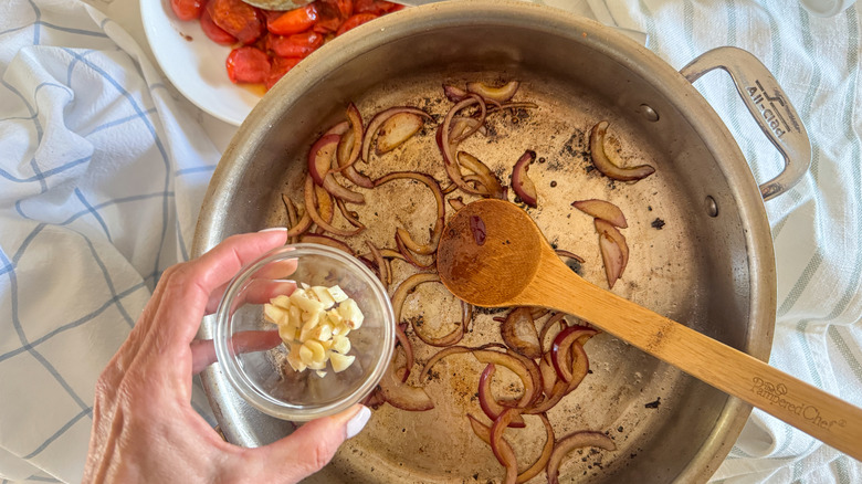 hand adding garlic to pan