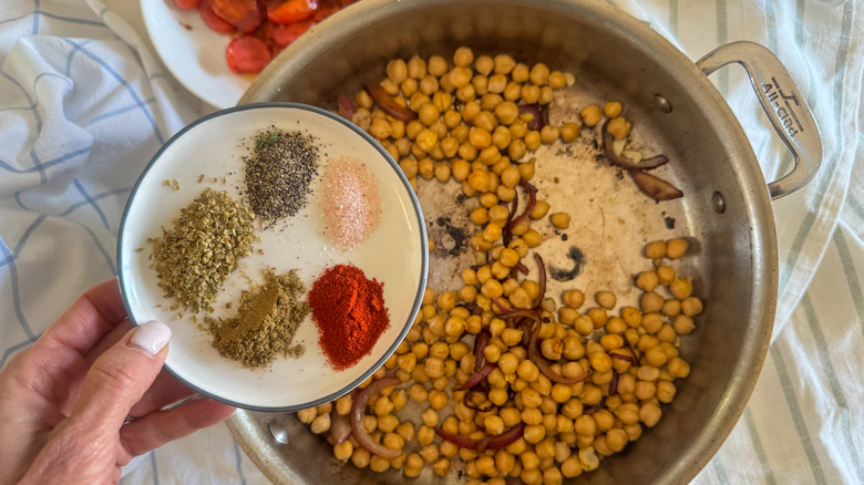 hand adding spices to pan