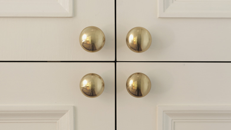 Four brass cabinet handles on white cabinet doors