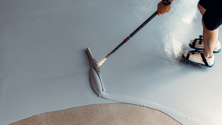 A construction worker applying grey coating to the floor