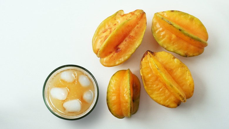 Glass of carambola juice with ice cubes next to carambola fruits