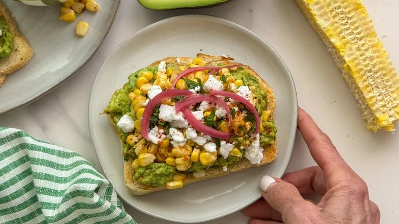 Hand holding dish of elote-topped avocado toast