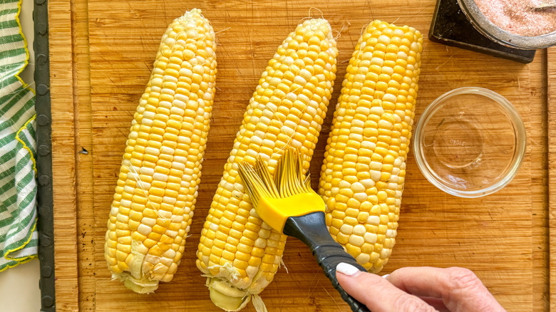 hand brushing corn with oil
