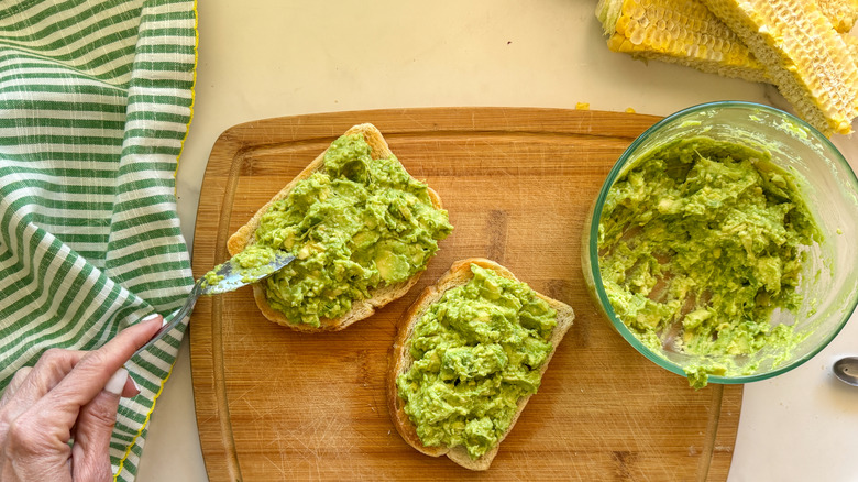 hand adding avocado to toast