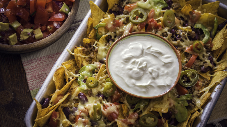 Sheet pan of nachos with a dish of sour cream in the center