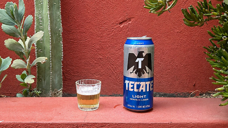 A can of Tecate Light sitting next to a filled glass of beer