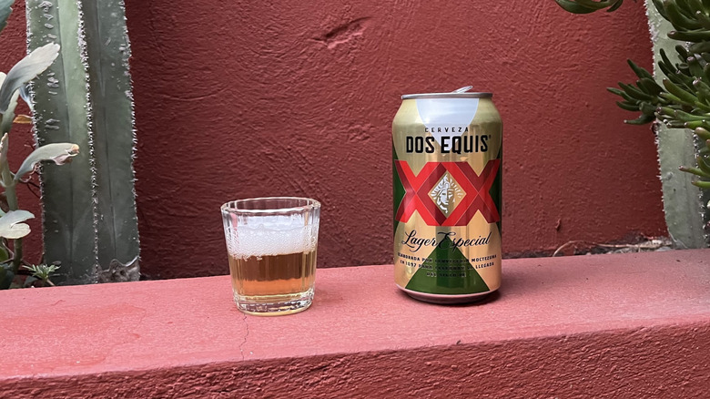 A can of Dos Equis sitting next to a filled glass of beer