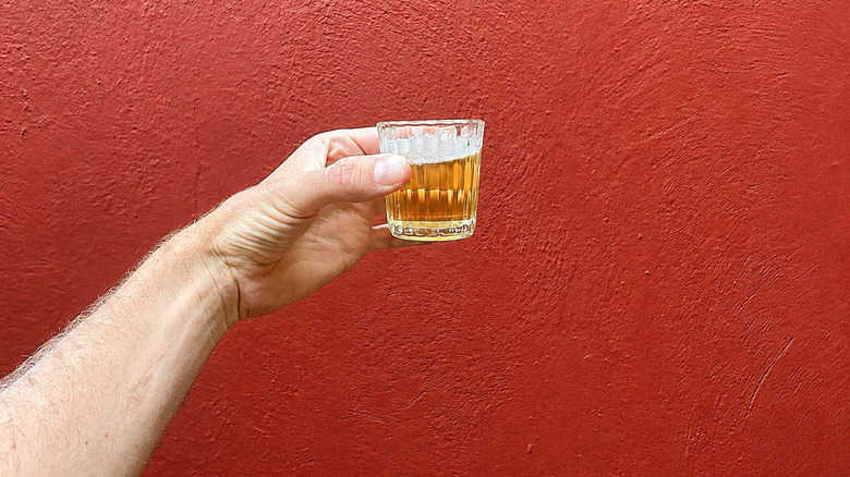 A hand holding up a little glass of beer