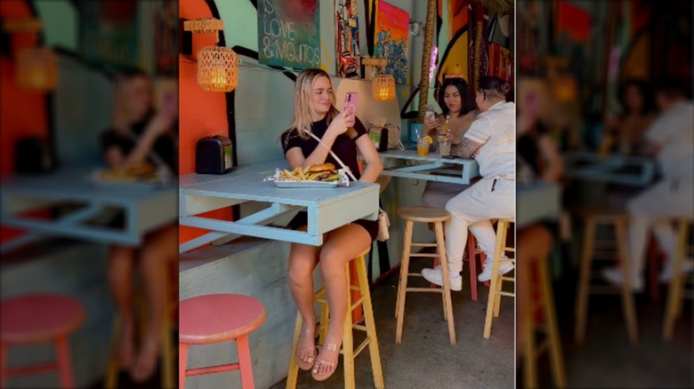Girl at Miami Mojito Company with hamburger and fries taking photo with phone
