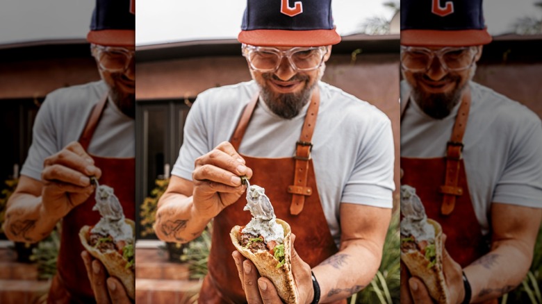 Michael Symon wearing hat and apron putting sauce on gyro