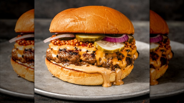 Burger topped with grainy mustard, cheese, pickles, and red onion