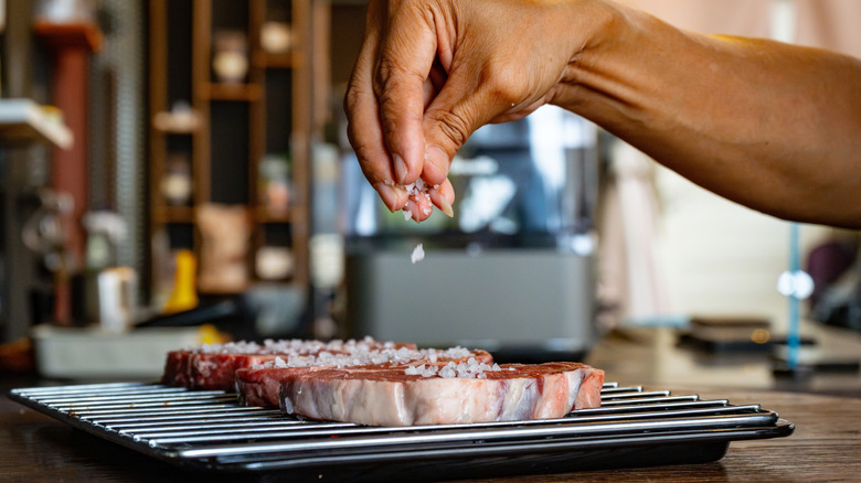 hand sprinkling coarse salt onto steaks