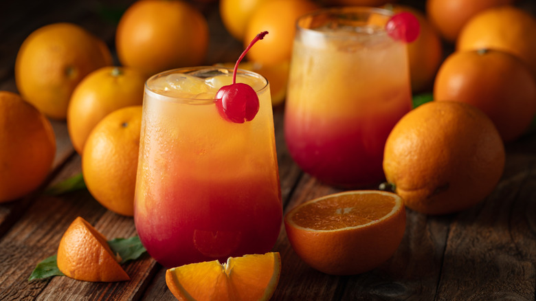 Two glasses of the Tequila Sunrise cocktail, surrounded by fresh oranges