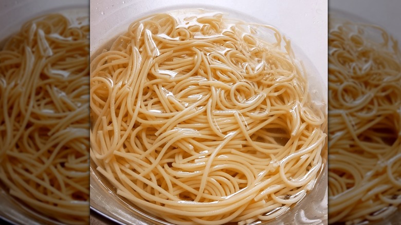 Cooked spaghetti in a glass bowl full of water