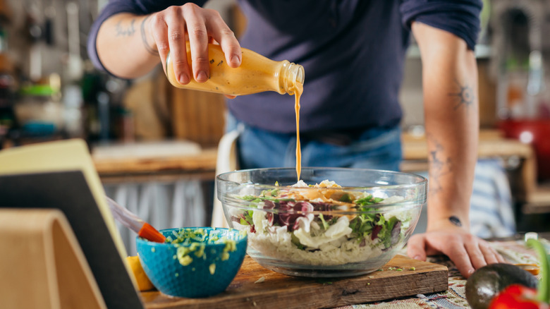 man pouring dressing on salad