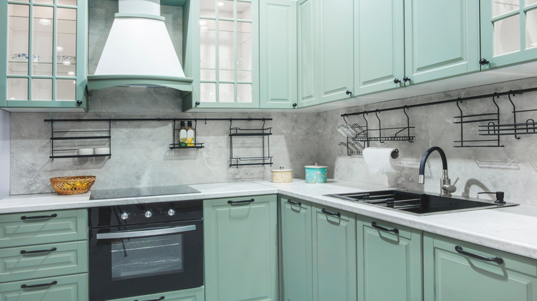 Kitchen with mint green cabinets, light stone countertops, and black hardware.