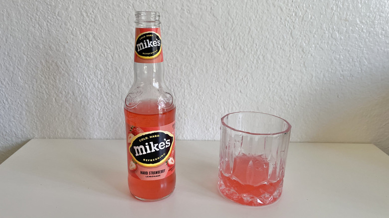 Open bottle of Mike's Hard Strawberry on a table next to a glass