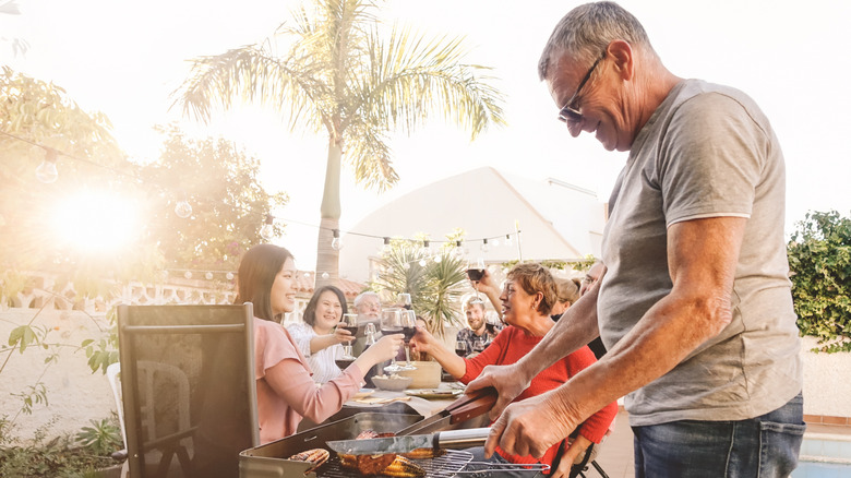 older man grilling meat for family