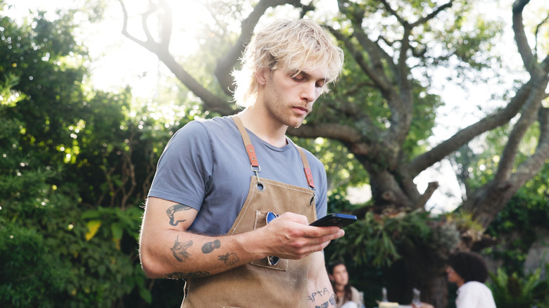 millennial man with bbq apron looking at phone