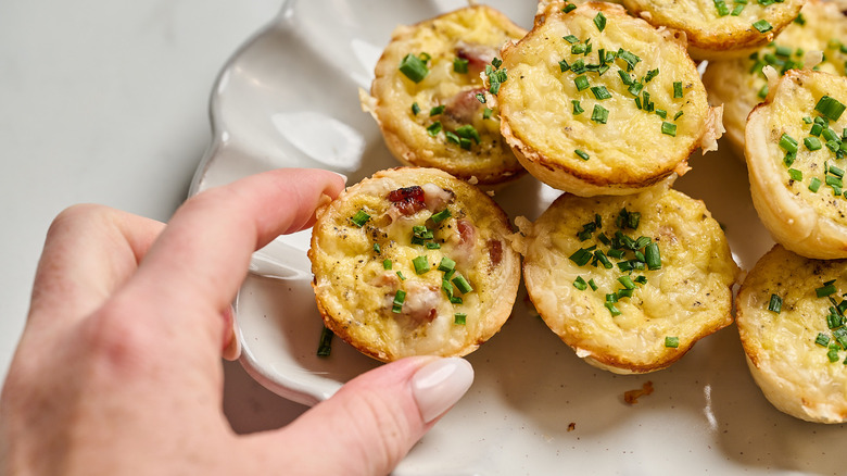 hand picking up a mini quiche cup from platter