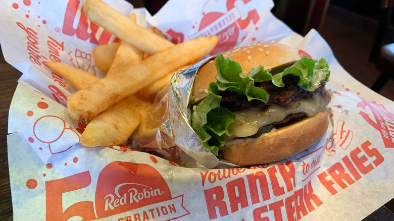 A Red Robin burger and steak fries, resting on greaseproof paper branded with the company logo