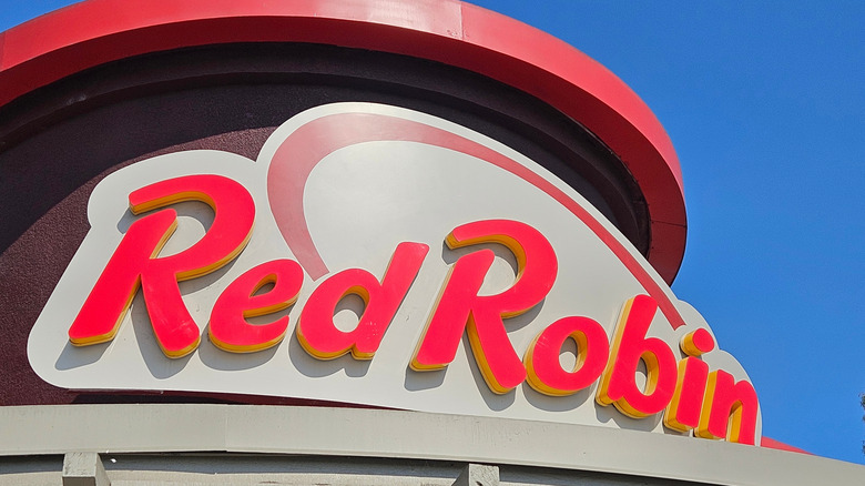 The exterior sign of a Red Robin restaurant location against the backdrop of a blue sky in daytime