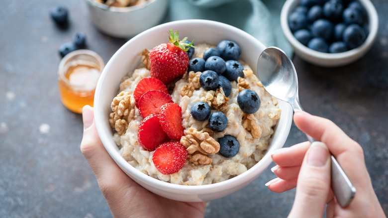 Someone holding a bowl of oatmeal with blueberries and strawberries with more ingredients in the background