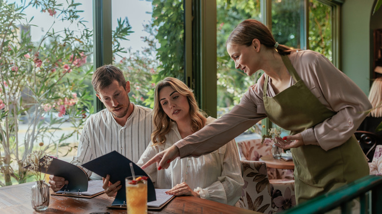 Waitress explaining menu to man and woman in restaurant