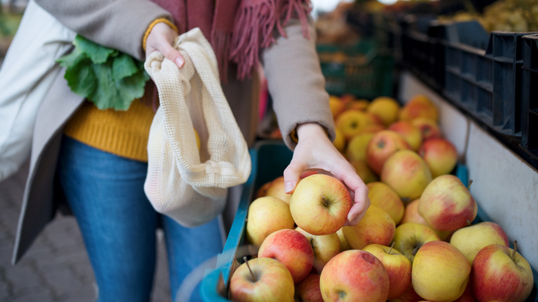 Person putting apples in reusable bag at farmers market