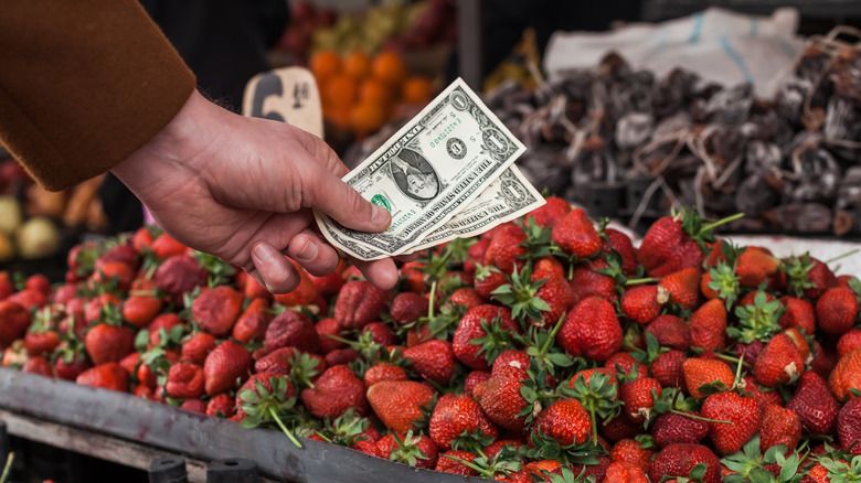 Person holding cash in front of strawberries at farmers market