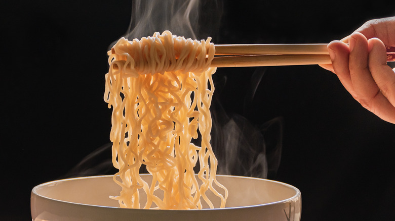 steaming ramen hanging off chopsticks over a bowl