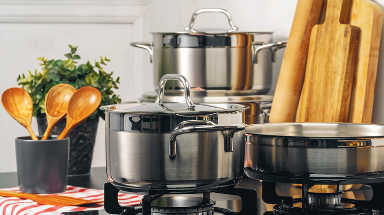 Stainless-steel pots and pans on a gas stove and counter, with cutting boards and a set of wooden spoons nearby