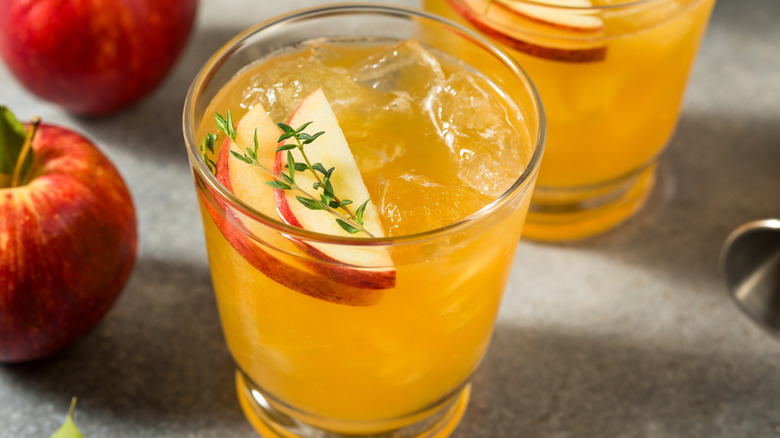A fall apple cider cocktail, with another drink in the background, along with two red apples