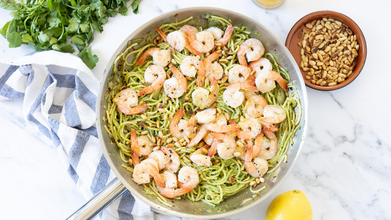 Mixed herb pesto shrimp pasta recipe on marble with herbs and lemon around.