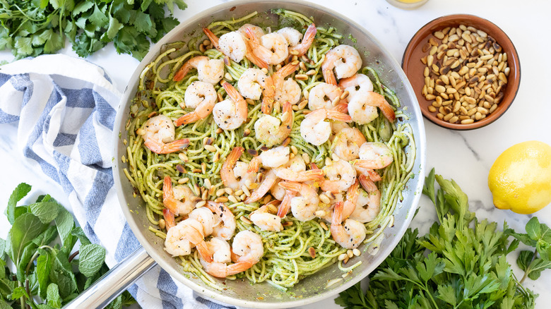 Mixed herb pesto shrimp pasta recipe on marble with herbs and lemon around.