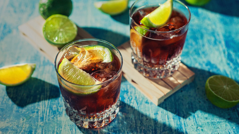 Two rum and cokes against a blue table